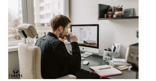 young male setting at a work desk drinking a cup of coffee