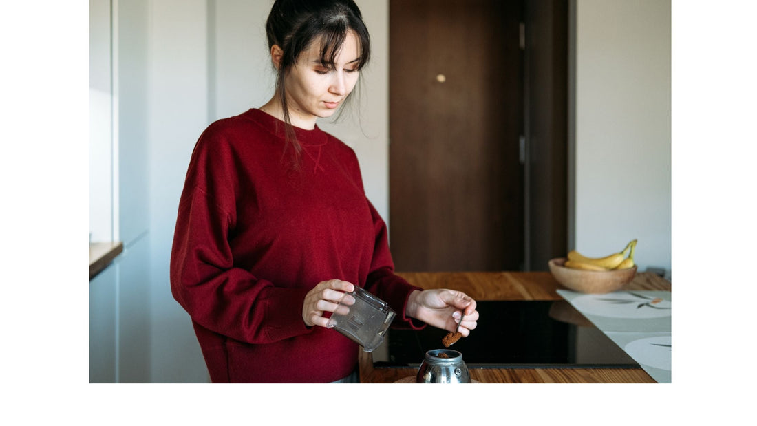 health concious woman in burgandy sweater making coffee bowl of ripe bananas in the background