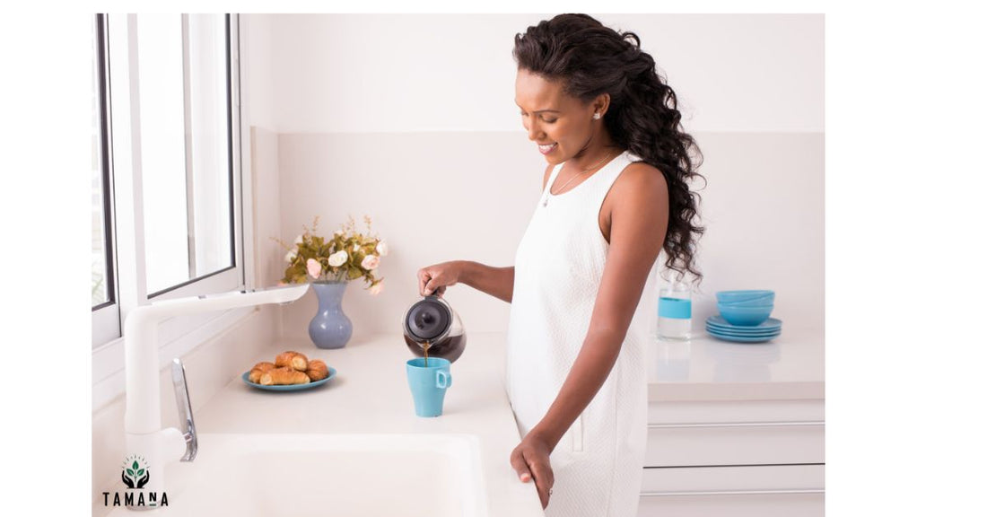 young female wearing all white standing in a white kitchen pouring coffee from a glass mug into a blue cup